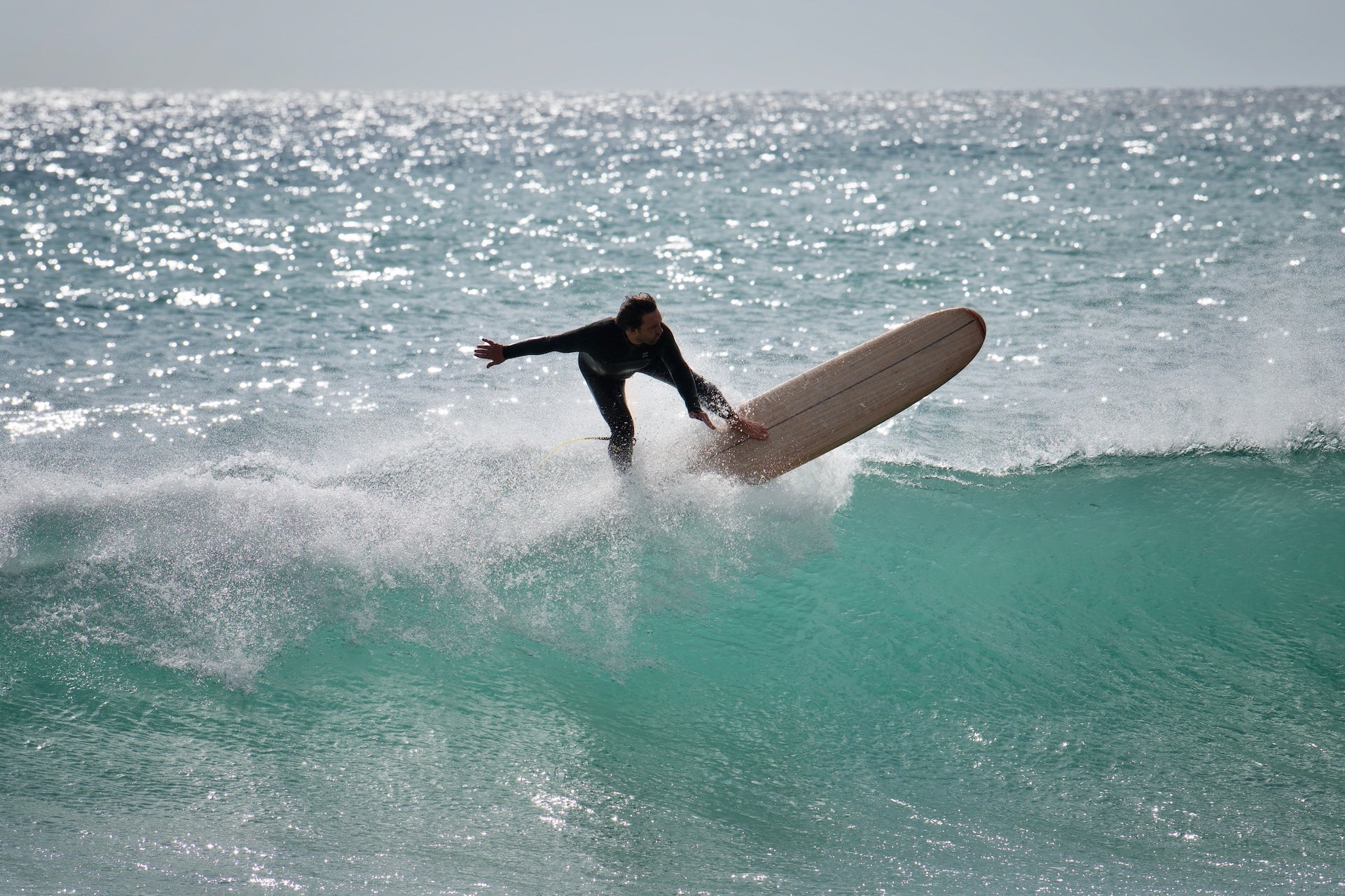 un surfeur en train faire un virage en haut de vague avec une planche en surf en bois